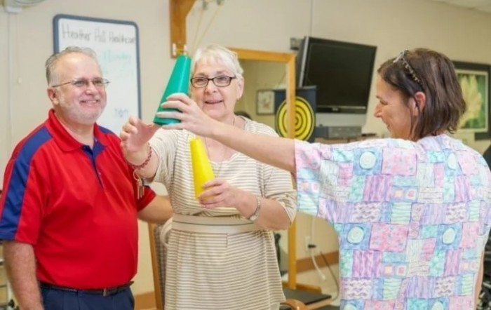 A therapist guides elderly individuals through a physical therapy exercise using cones.