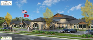 A scenic view of a modern building with stone accents, surrounded by landscaping, and a parking lot with cars and people nearby.
