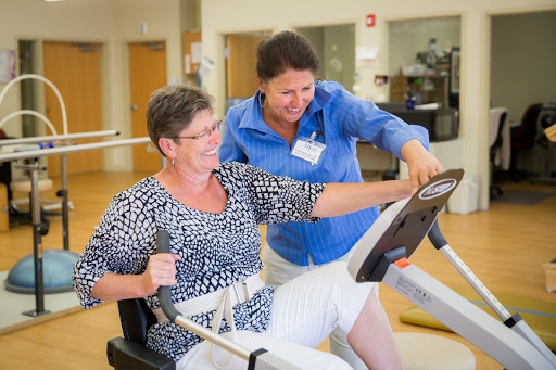 A physical therapist assists an older woman during a workout session, promoting health and fitness.