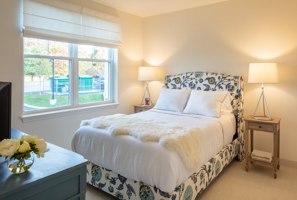 A cozy bedroom with a patterned bed, soft lighting, and a window view.