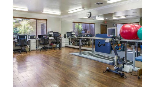 A well-equipped therapy room featuring exercise equipment and a spacious, bright interior.