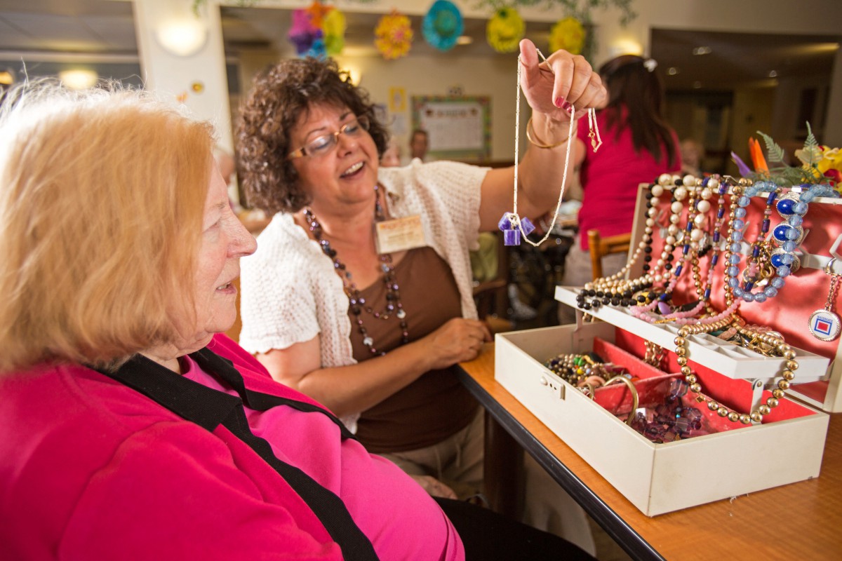Two women enjoy looking at a collection of jewelry during an indoor social event.
