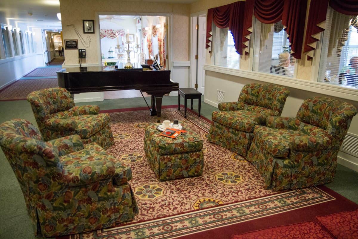 A cozy living room featuring patterned armchairs, a piano, and an ornate carpet.