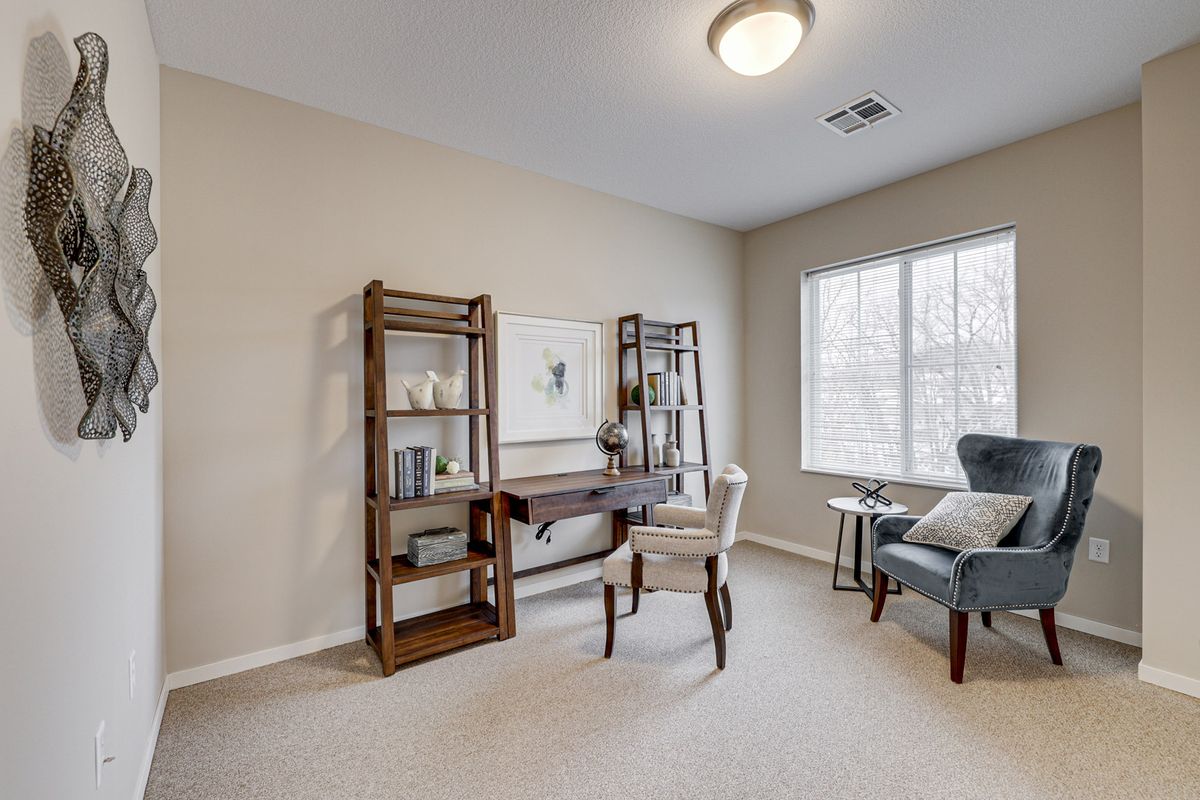 A cozy home office with a wooden desk, bookshelves, and a comfortable chair by the window.