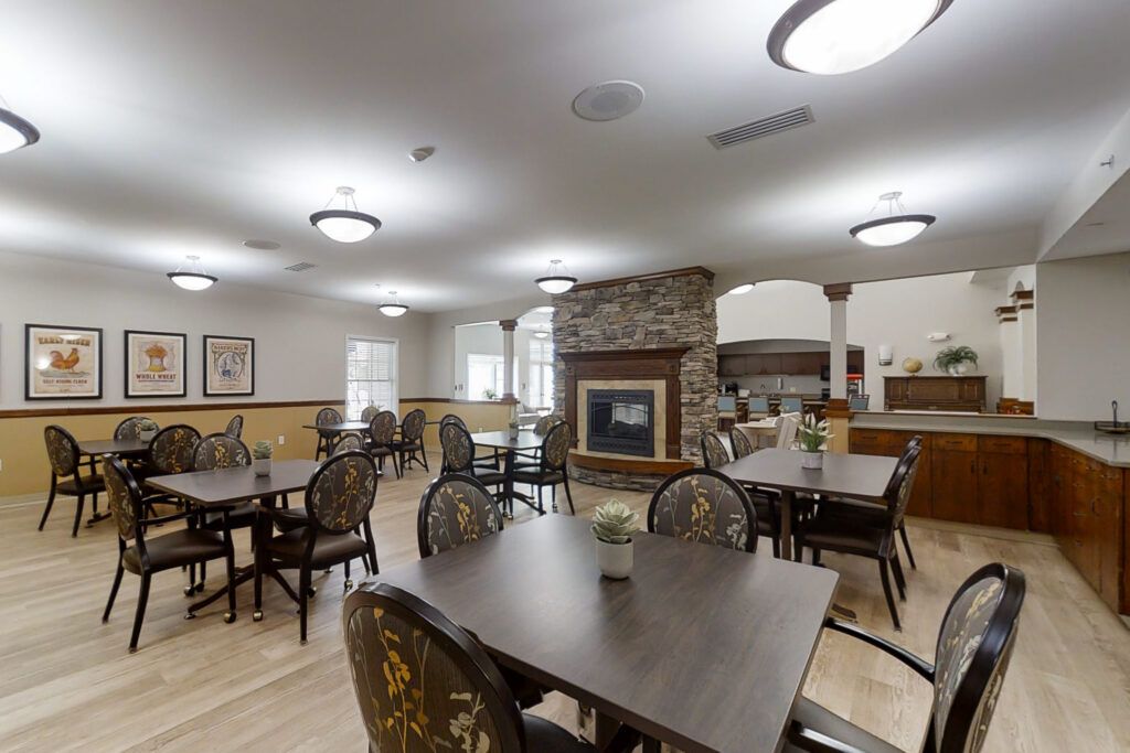 A well-lit dining room with multiple tables and chairs, featuring a central fireplace.