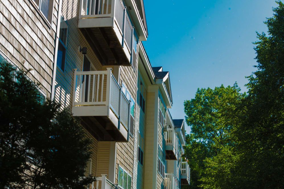 A residential apartment building with balconies against a clear blue sky and surrounded by trees.