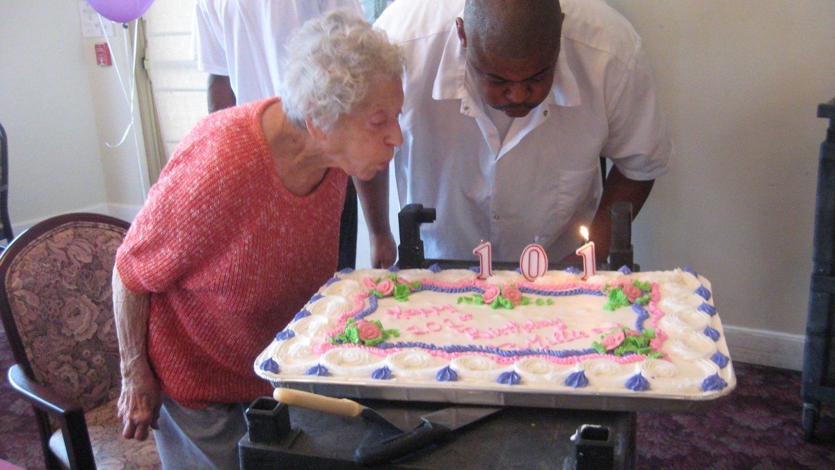 An elderly woman blowing out candles on a birthday cake with the number 101.