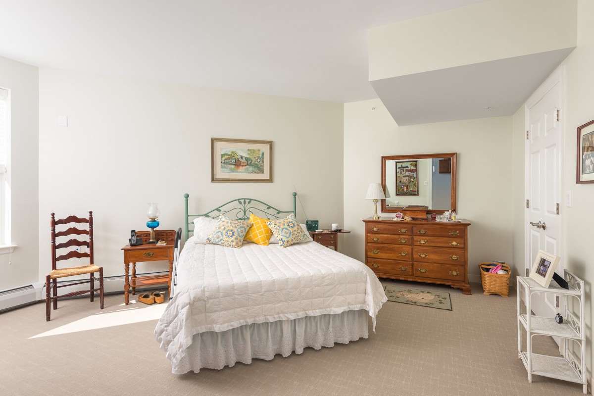A cozy bedroom featuring a bed with decorative pillows, wooden dressers, and a large mirror.
