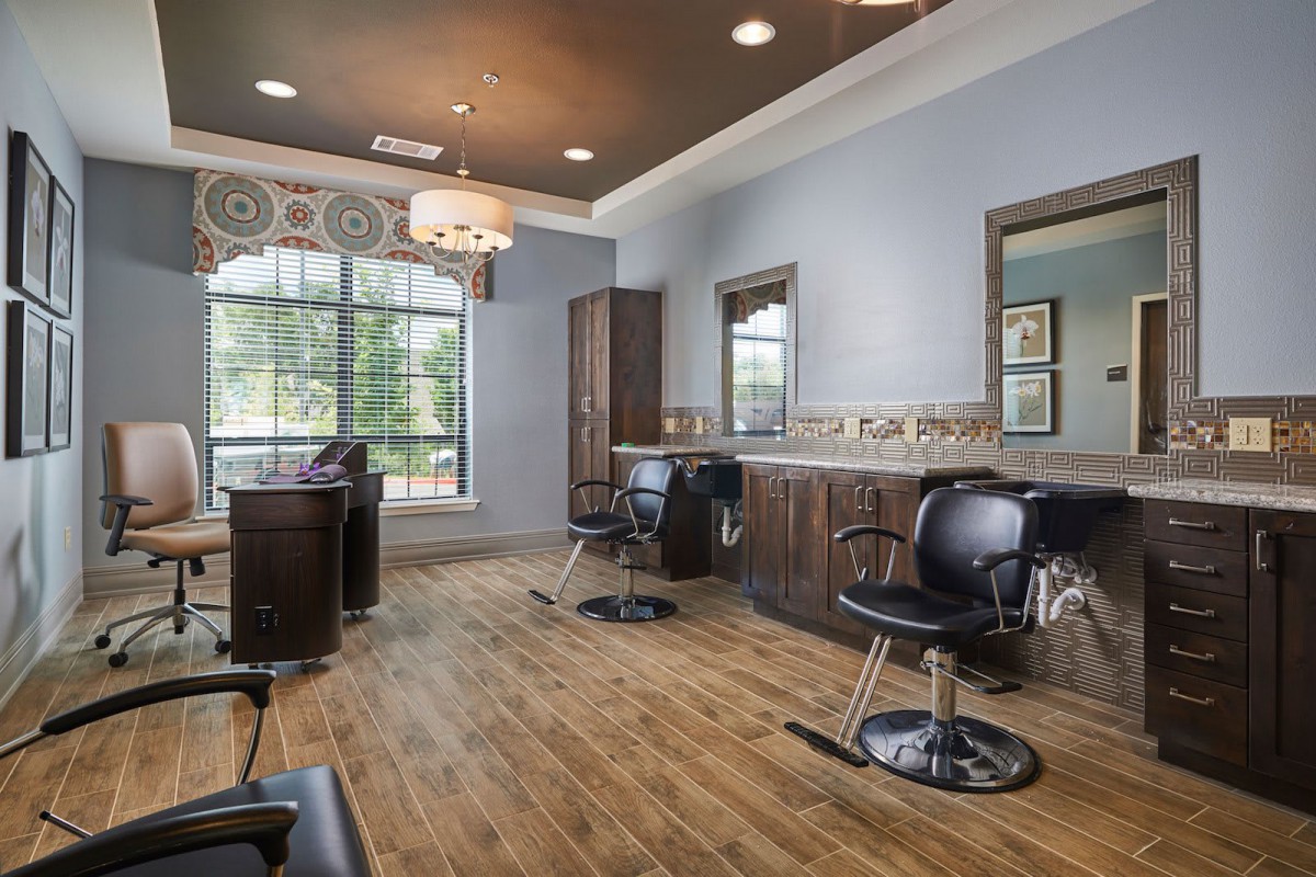 A stylish hair salon interior with modern chairs and large mirrors, featuring elegant wood flooring and natural light from a large window.