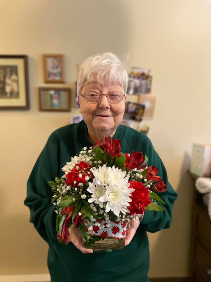 An elderly woman holding a bouquet of red and white flowers indoors.