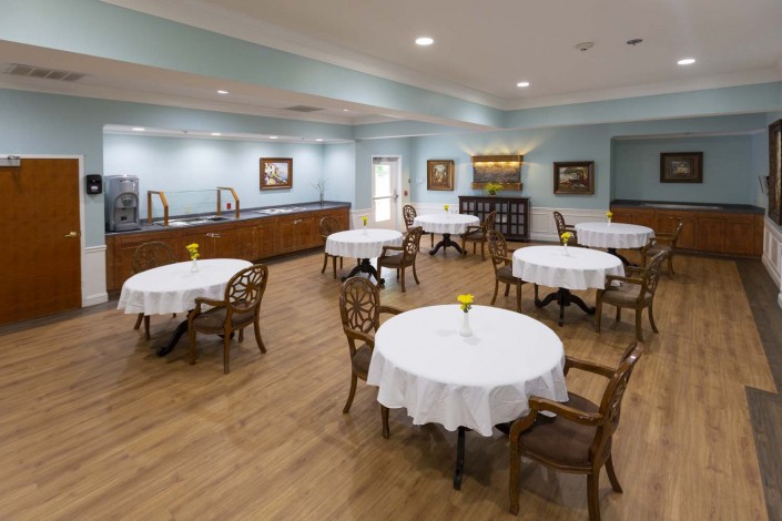A well-lit dining room with round tables and wooden chairs, featuring elegant decor.