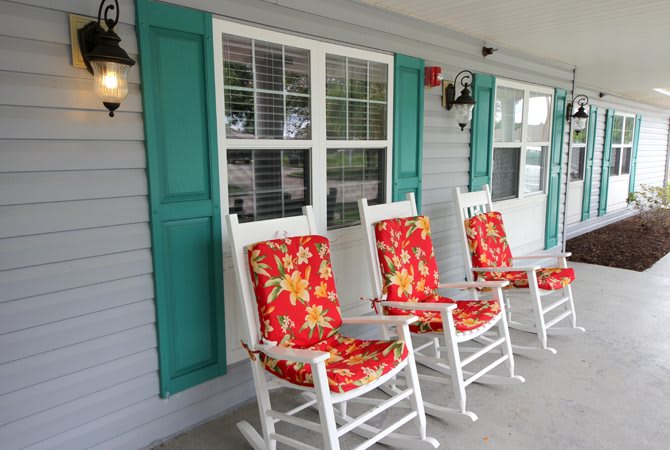 A row of white rocking chairs with bright floral cushions on a porch with teal shutters.