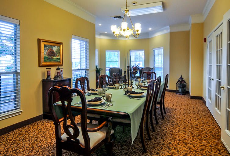 A formal dining room with a long table set for a meal, featuring elegant chairs and a chandelier.