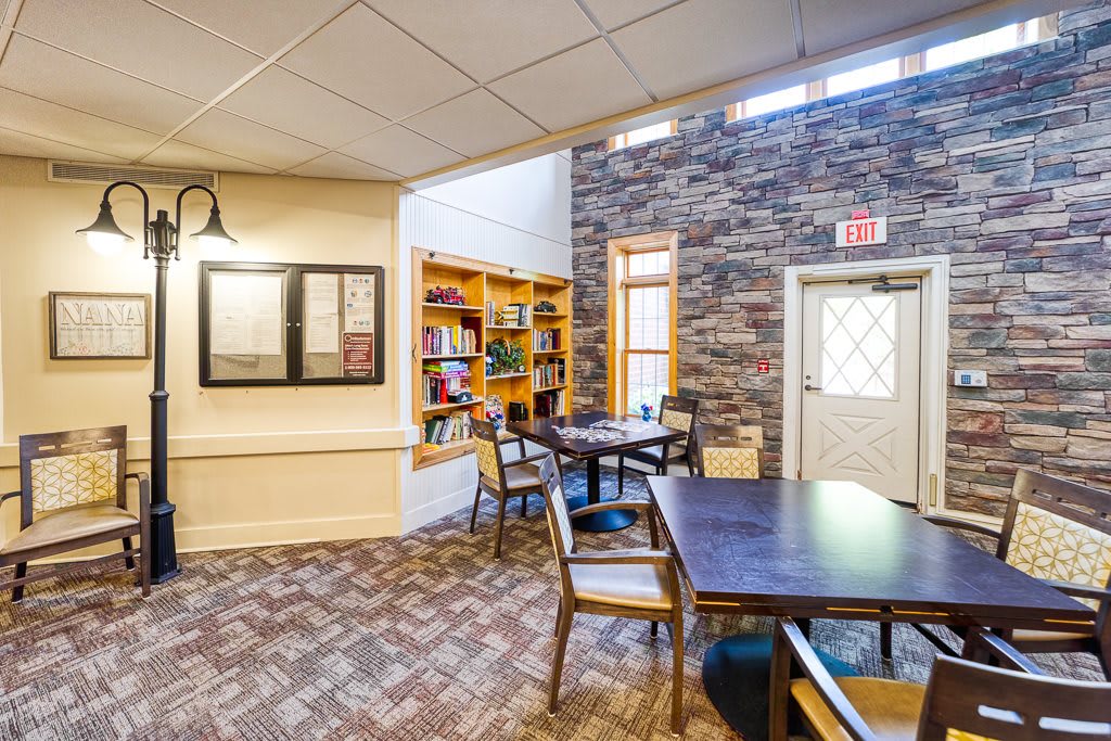 A cozy reading area with tables, chairs, and a bookshelf against a brick wall.