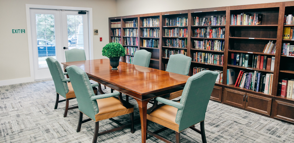 A cozy library meeting room with a wooden table, chairs, and bookshelves filled with books.