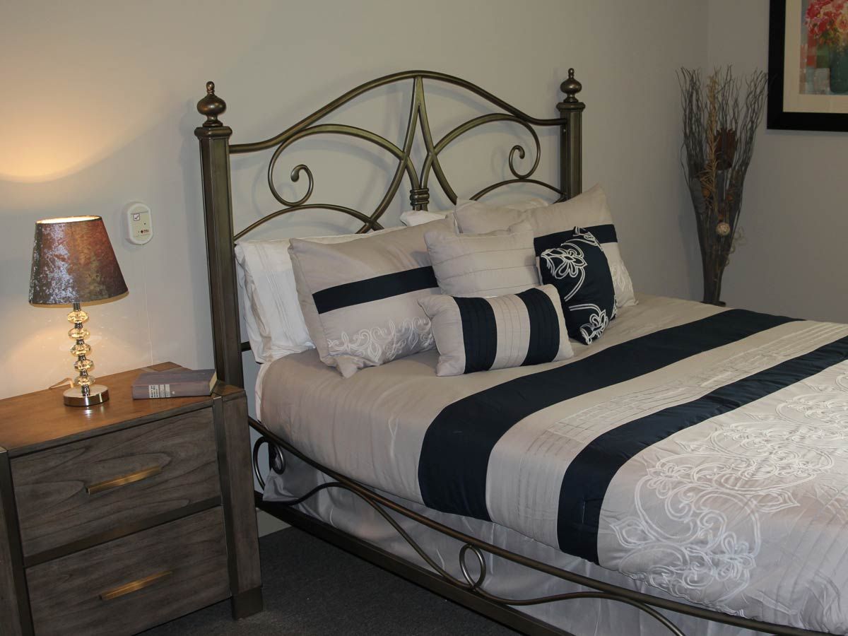 A cozy bedroom with a decorative metal headboard, patterned bedding, and a bedside lamp.