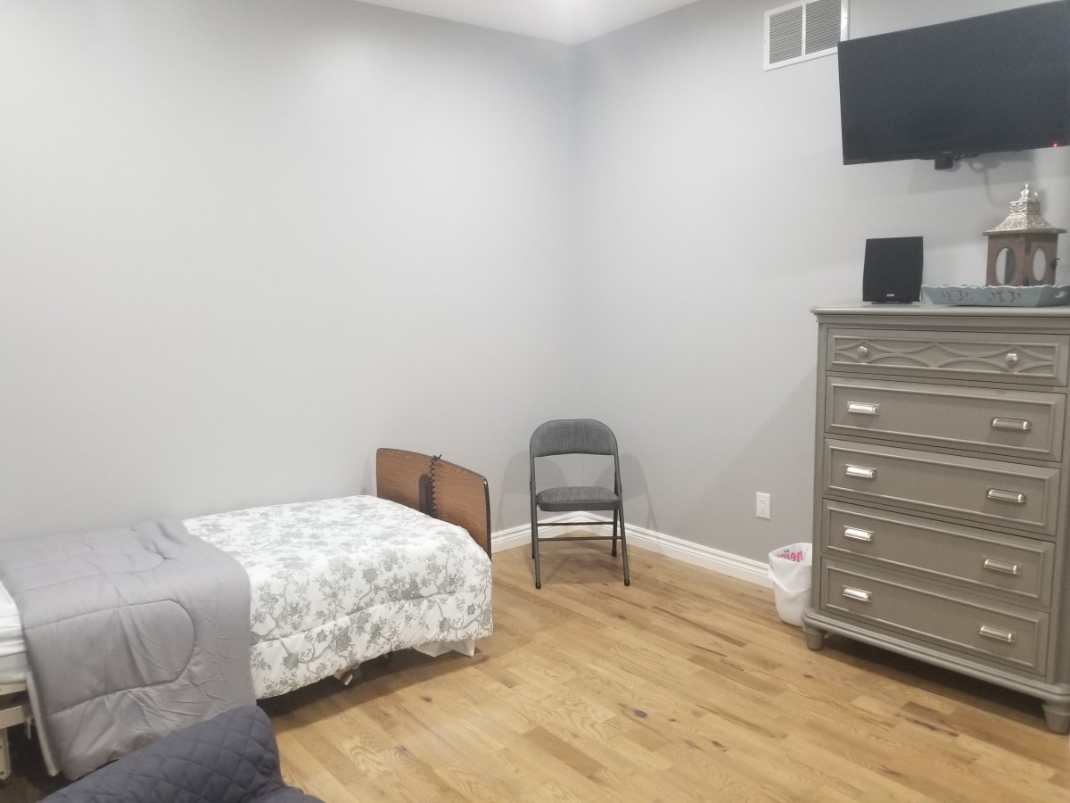 A minimalist bedroom featuring a single bed, chair, dresser, and a wall-mounted television.