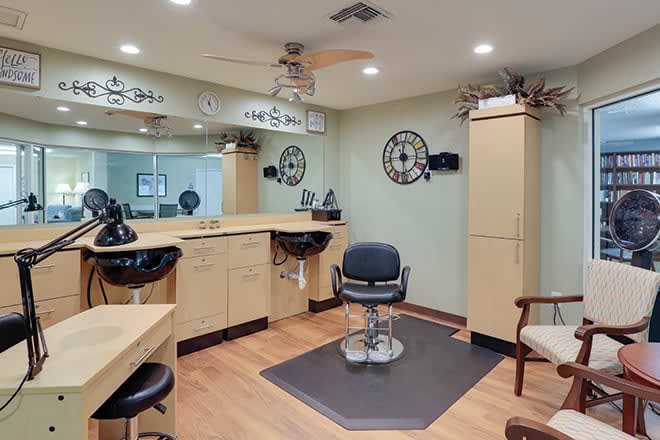 A well-organized hair salon interior featuring a barber chair, large mirrors, and ample cabinetry.