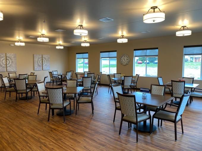 An empty dining room with neatly arranged tables and chairs, featuring large windows and overhead lighting.