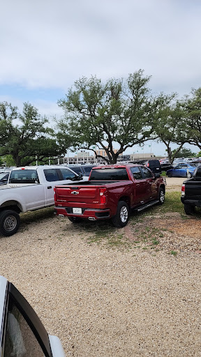 A red pickup truck parked among other vehicles in a grassy area with trees.