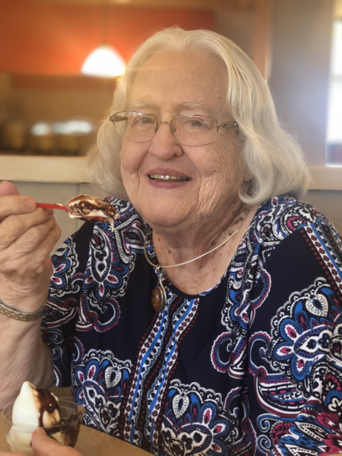 An elderly woman enjoying ice cream while smiling.