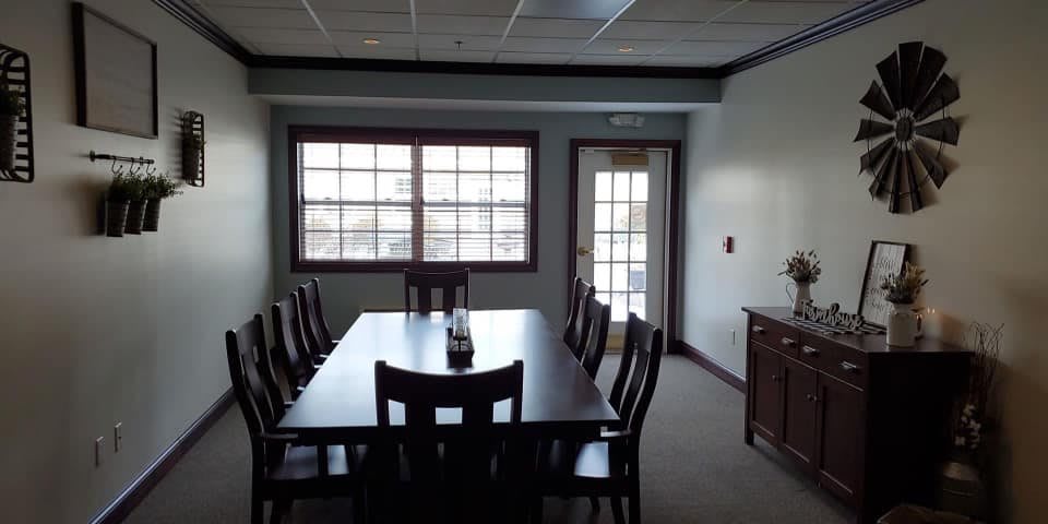 A conference room with a large table and chairs, featuring a window and door.