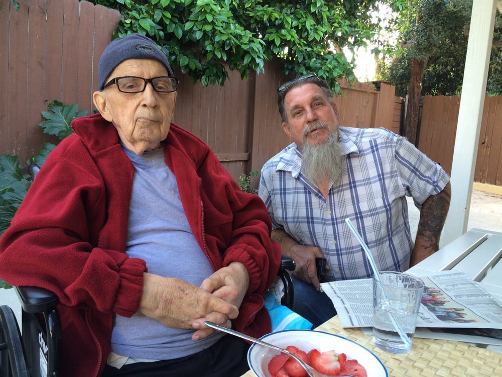 Two people sitting outdoors with a bowl of fruit on the table.