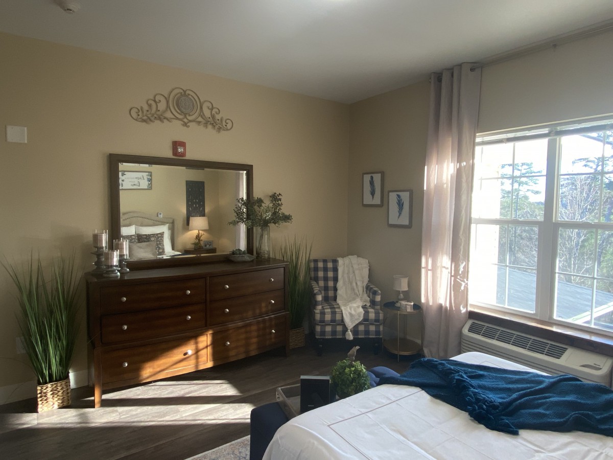 A cozy bedroom with a dresser and mirror, featuring a comfortable chair by the window.