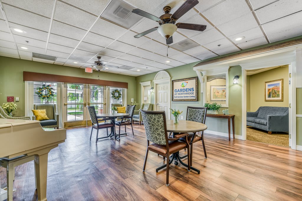 A cozy dining area with tables and chairs, featuring ceiling fans and large windows for natural light.