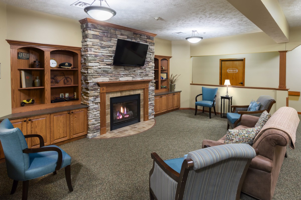 A cozy living room with a fireplace, armchairs, and a wall-mounted television.