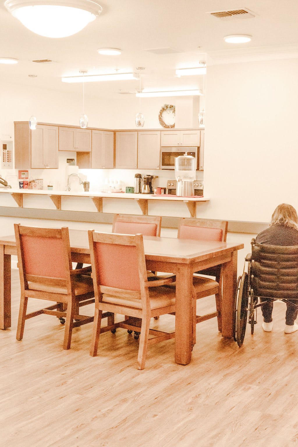 A cozy kitchen and dining area with a wooden table, chairs, and a person in a wheelchair.
