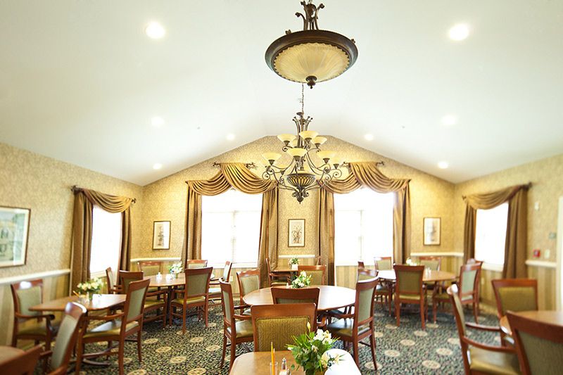 An elegant dining room featuring a large chandelier, multiple tables and chairs, and richly decorated curtains.