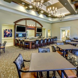 A well-lit dining and bar area featuring multiple tables, chairs, chandeliers, and televisions.