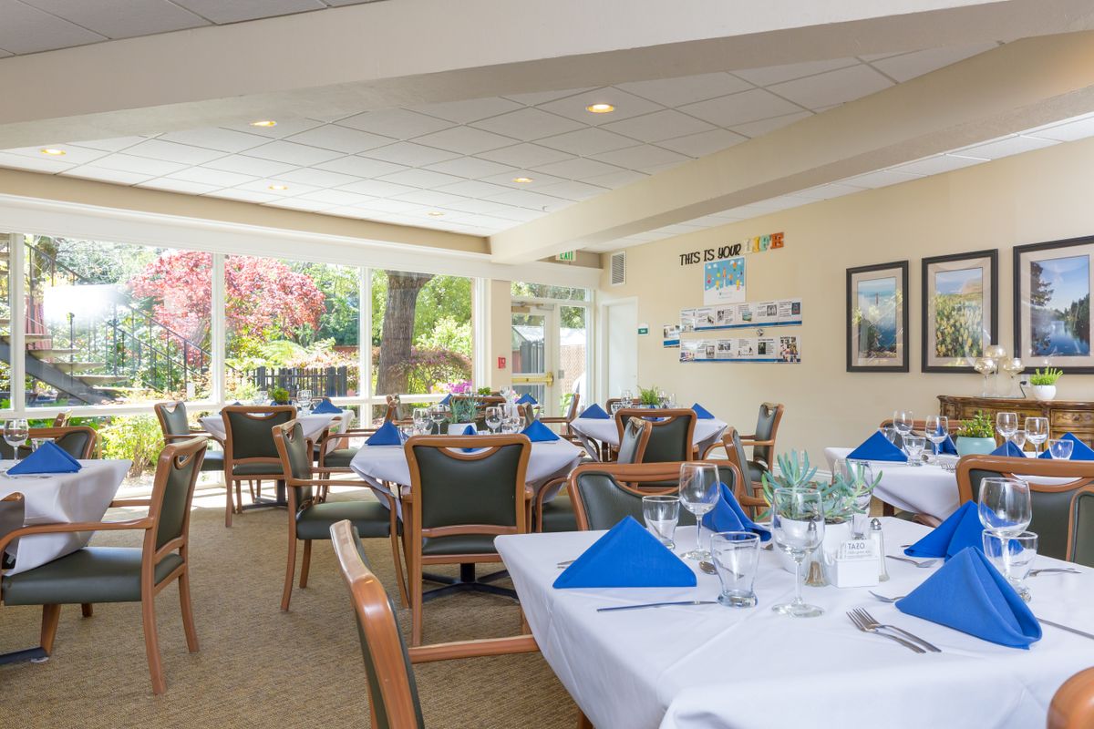A well-lit dining room with neatly arranged tables and blue napkins.