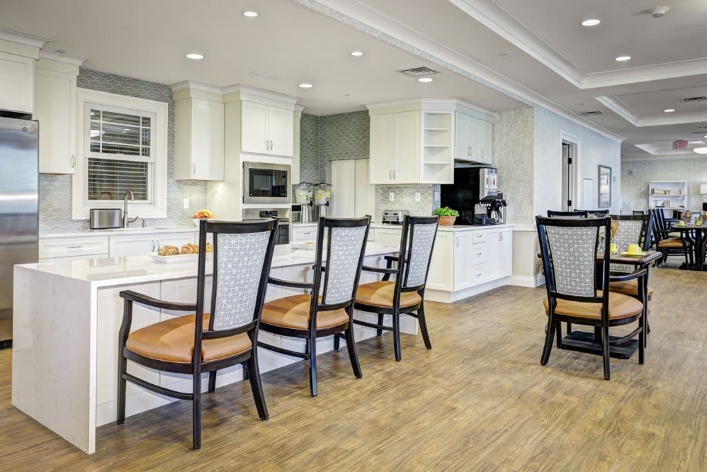 A modern kitchen with white cabinets and a wooden floor featuring an island countertop and dining chairs.