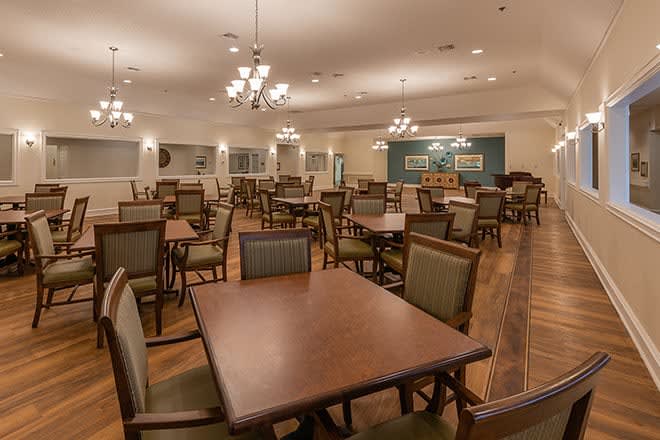 An empty dining room with neatly arranged tables and chairs, featuring elegant lighting and wood flooring.