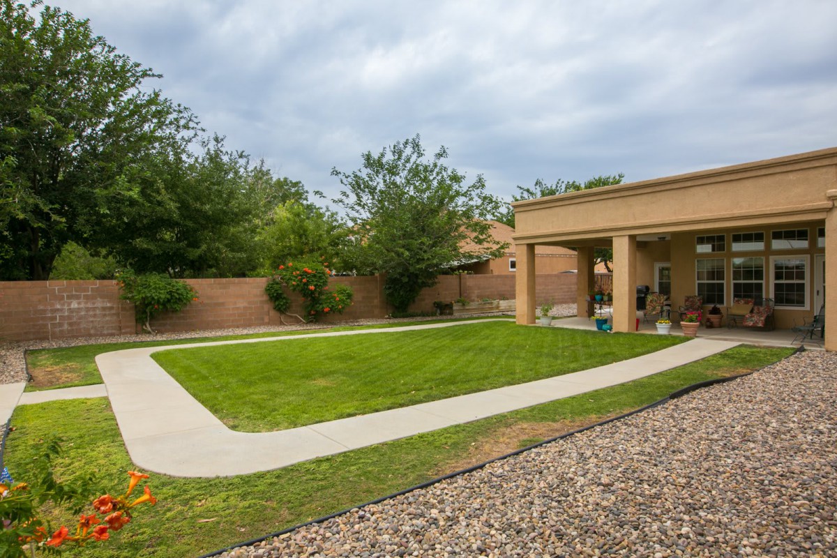 A neatly maintained backyard with a lush lawn, patio area, and surrounding garden.