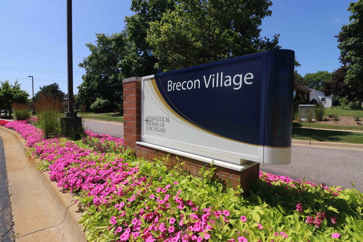 Entrance sign for Brecon Village surrounded by vibrant flowers.