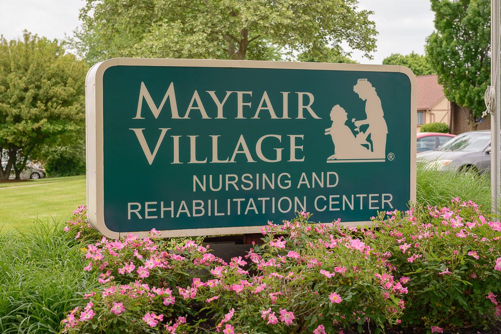 Sign for Mayfair Village Nursing and Rehabilitation Center surrounded by flowers.