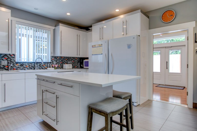 A modern kitchen interior featuring white cabinets, a central island with stools, and contemporary appliances.