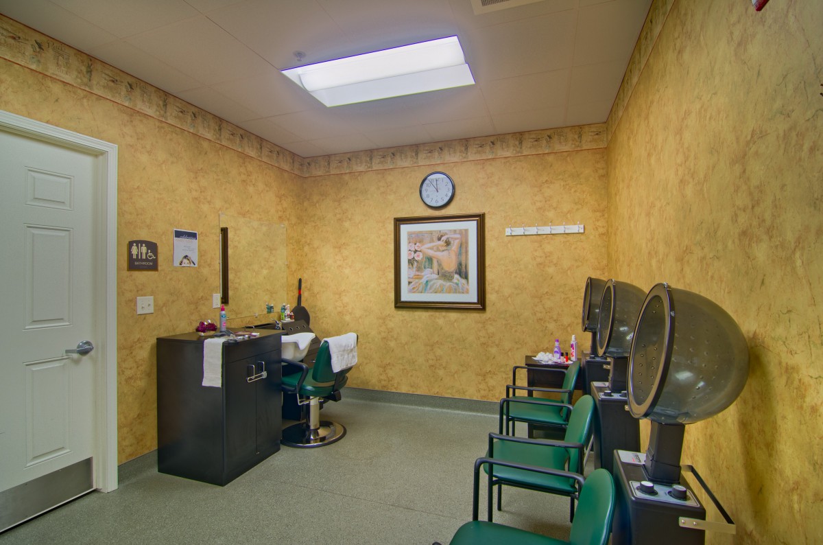 A small waiting room with green chairs and a desk, featuring wall art and a clock.