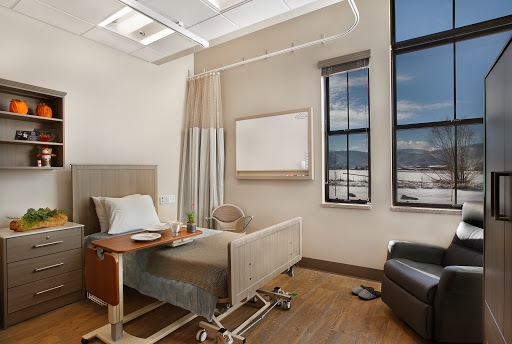A modern hospital patient room featuring a bed, ample natural light from large windows, and a comfortable sitting area.