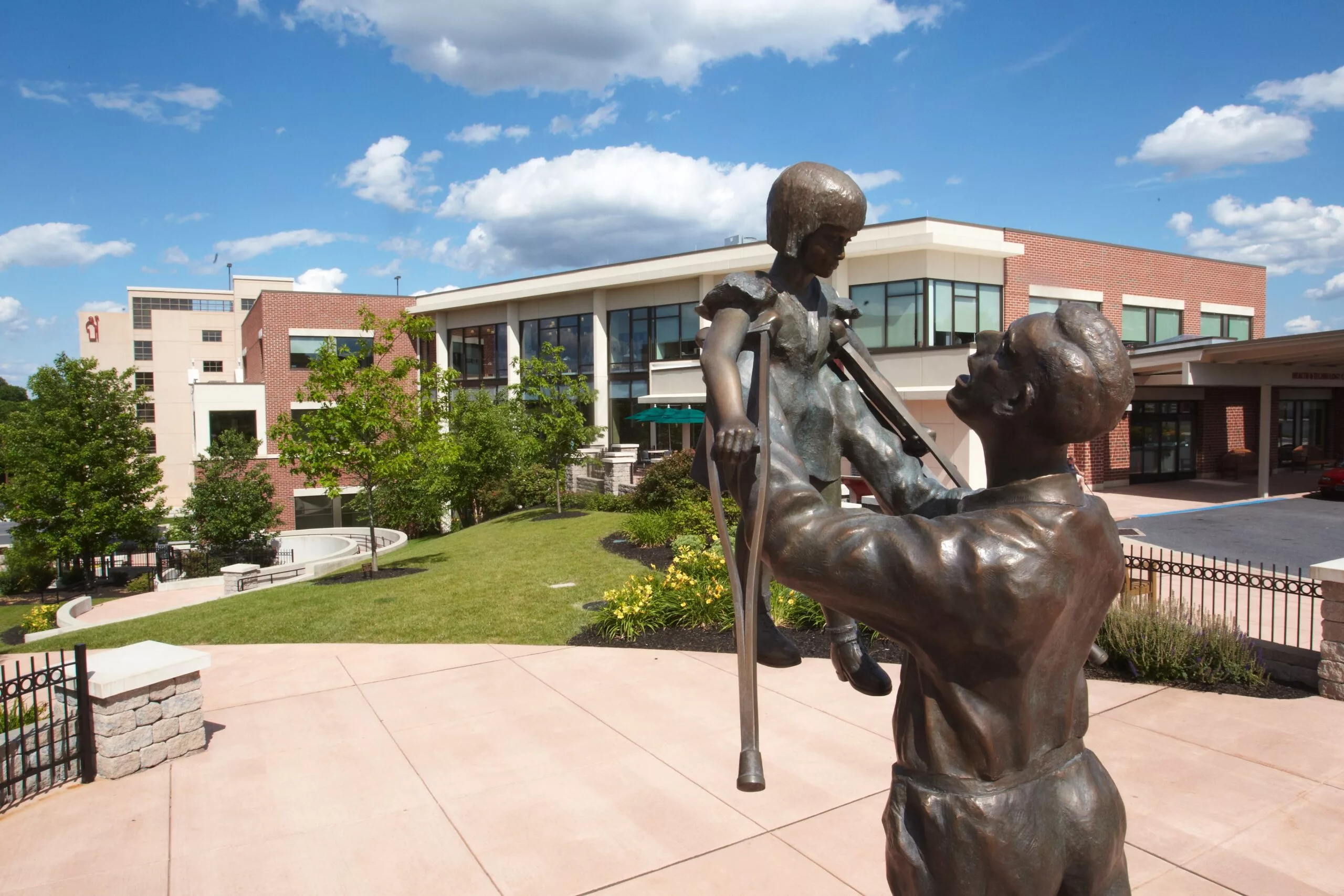 A sculpture outside a modern building on a sunny day with blue skies and clouds.