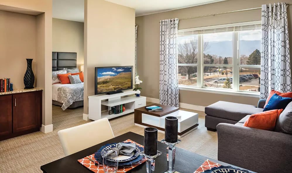 A modern open-concept living space with a dining area and an adjacent bedroom, featuring stylish decor and ample natural light.