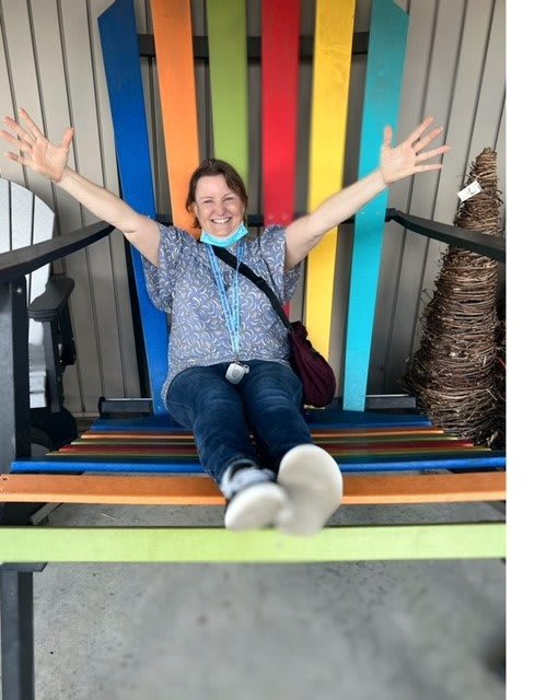 A person joyfully sitting on a colorful giant chair with arms outstretched.