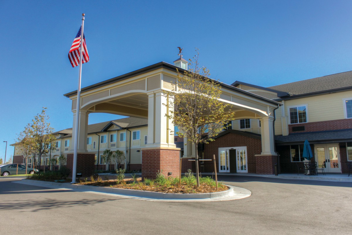 A modern building entrance with an American flag flying nearby under a clear blue sky.
