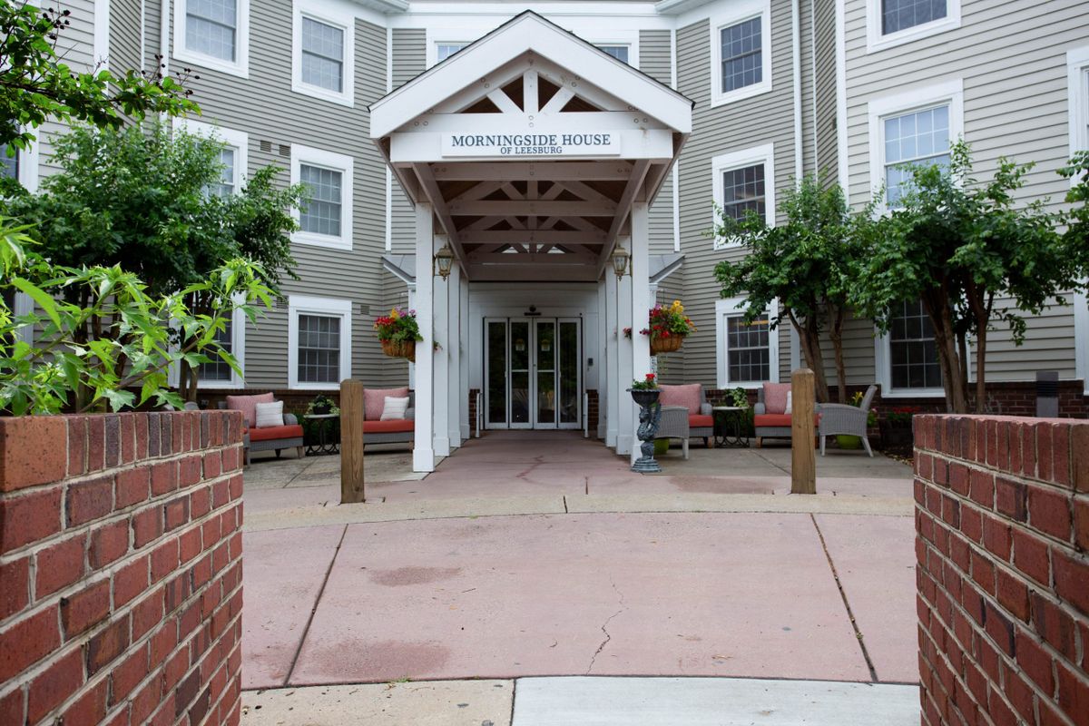 The entrance of a hotel featuring a covered porch and surrounding greenery.