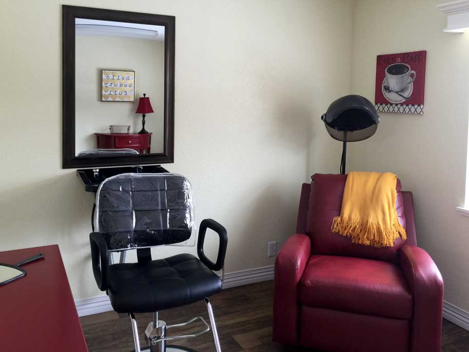 A cozy hair salon corner with a styling chair, mirror, and a vintage hair dryer next to a red sofa.