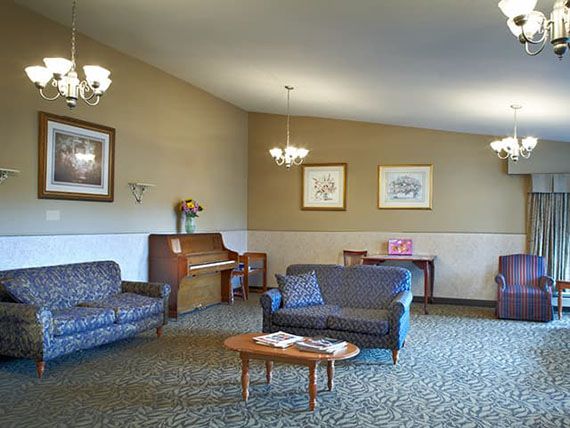 A cozy living room featuring a piano, sofas, and elegant chandeliers.