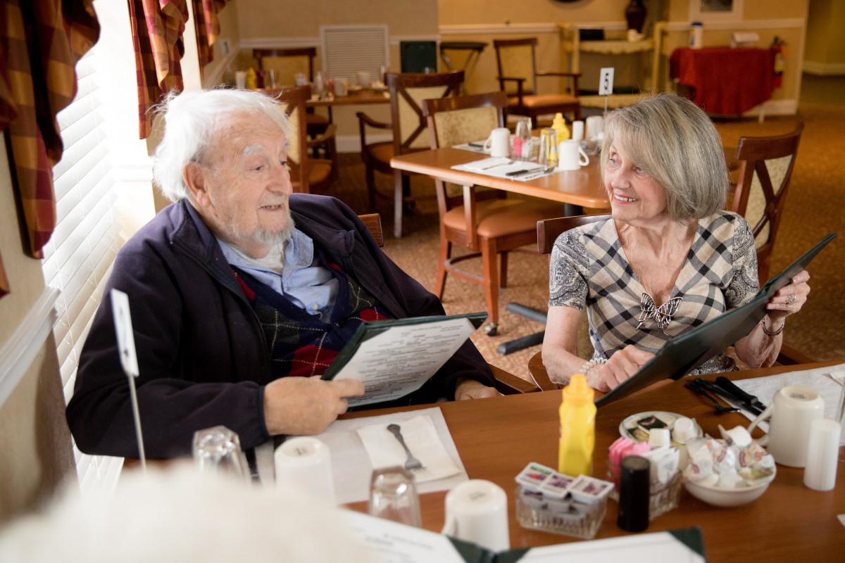 An elderly man and a woman are having a conversation in a restaurant while looking at the menu.